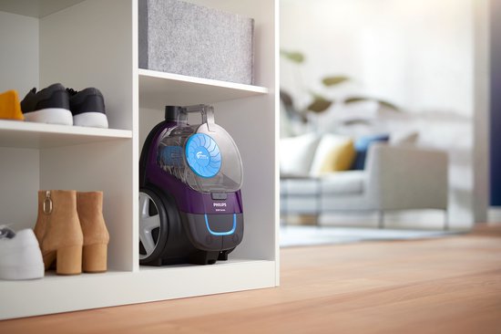 Aspirateur violet Philips dans une étagère blanche ouverte, à côté de chaussures et bottines.