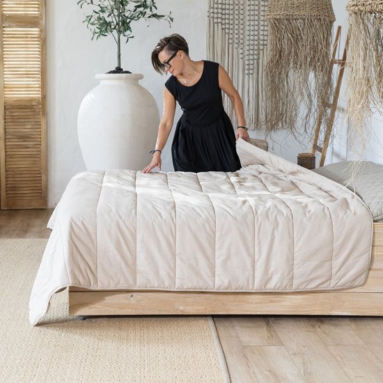 Vrouw met zwart jurkje en bril legt een beige hennep dekbed op een bed.