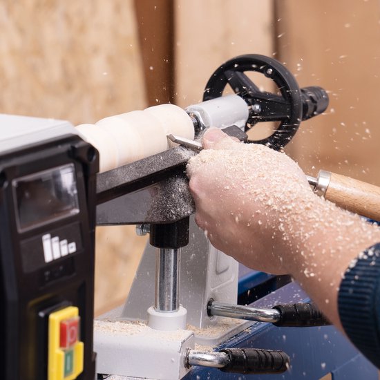 Gedetailleerde opname van een persoon die hout bewerkt met een blauwe Scheppach houtdraaibank. Houtsnippers vliegen in het rond.