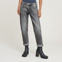 Model draagt een grijze jeans met opgerolde broekspijpen en zwarte laarzen.