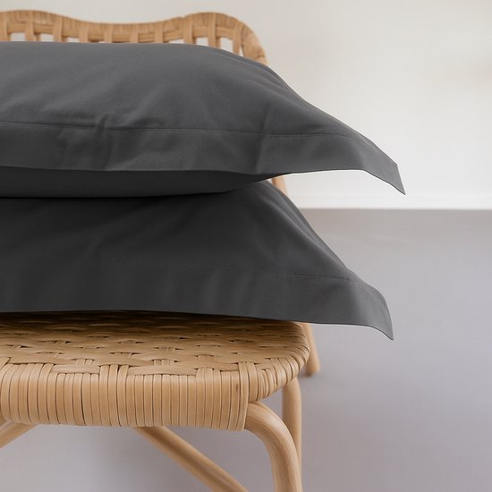 Deux taies d'oreiller gris foncé avec bordure Oxford, empilées sur une chaise en rotin.