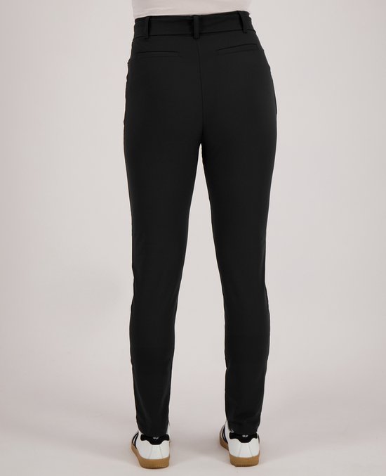 Zijaanzicht achterkant van een vrouw in een zwarte slim-fit broek en witte sneakers met strepen.
