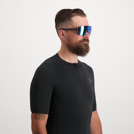 Man met baard draagt een zwarte fietsoutfit en een oversized fietsbril met spiegelende blauwe lenzen.