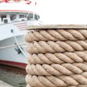 Cordes épaisses en jute brun enroulées autour d'un poteau sur un quai, avec un navire en arrière-plan.