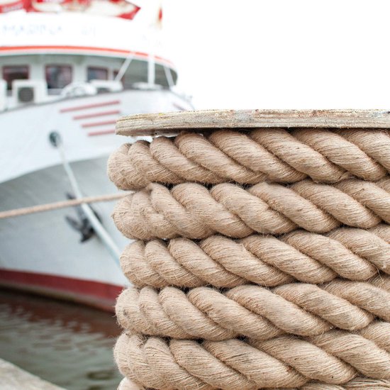 Cordes épaisses en jute brun enroulées autour d'un poteau sur un quai, avec un navire en arrière-plan.