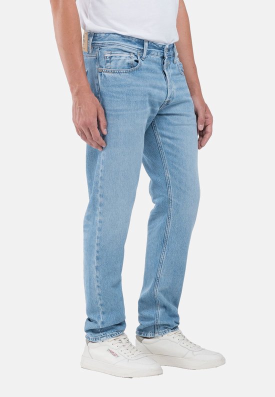 Homme en jean Replay bleu clair avec fermeture boutonnée, cinq poches et baskets blanches.