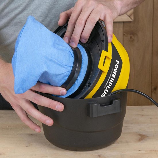 Een persoon plaatst een blauw stofzuigerzak in de zwarte tank van een gele Powerplus stofzuiger.