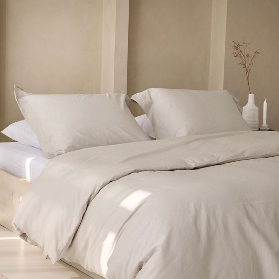 Een opgemaakt bed met een zandkleurig dekbedovertrek en kussens, in een lichte kamer.