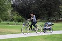 Vrouw op fiets met hondenbuggy in een park.