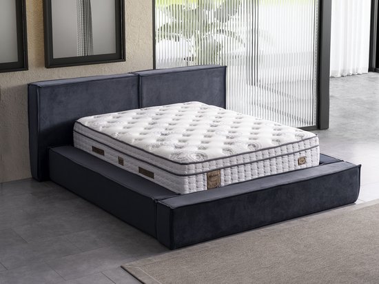 Matelas avec motifs blanc et gris sur un lit gris foncé avec tête de lit.