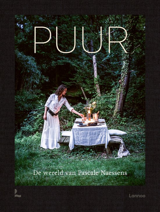 Boek "PUUR De wereld van Pascale Naessens" met een vrouw in een witte jurk bij een gedekte tafel in het bos.