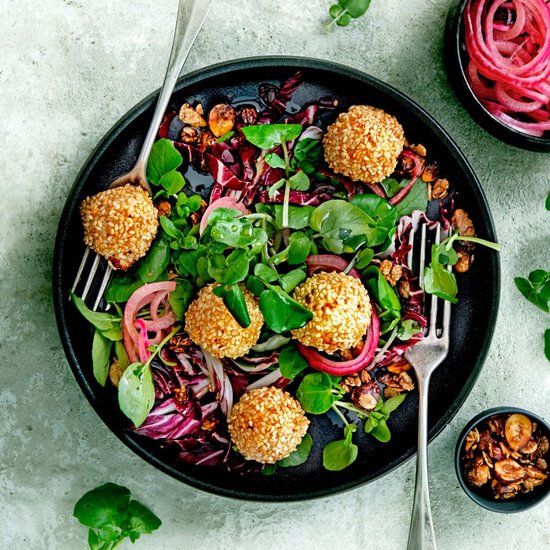 Zwarte schaal met salade van radicchio, rucola, ingelegde rode ui en sesamkoekjes.