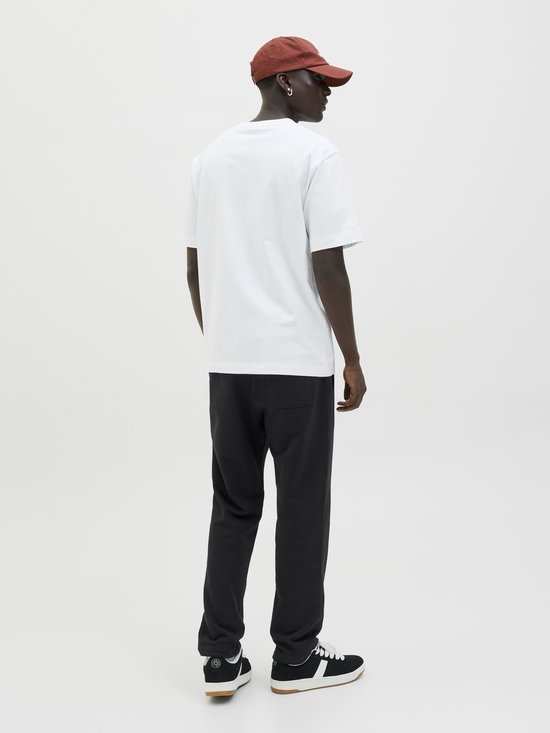 Man met witte t-shirt, zwarte joggingbroek en bruine pet, achterkant.