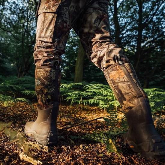 Persoon die bruine Muck Boot Woody Max laarzen draagt in een bosrijke omgeving.
