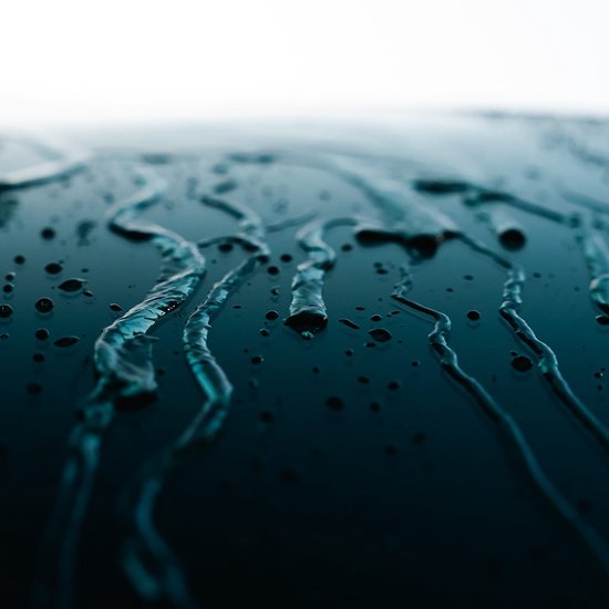 Close-up van waterdruppels en stromen op een glanzend, donker oppervlak, waarschijnlijk een auto.