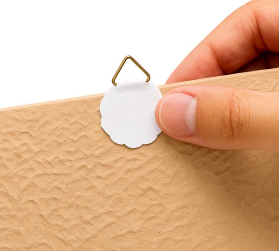 Hand bevestigt een wit, bloemvormig ophanghaakje aan de achterkant van een keramisch tegeltje.