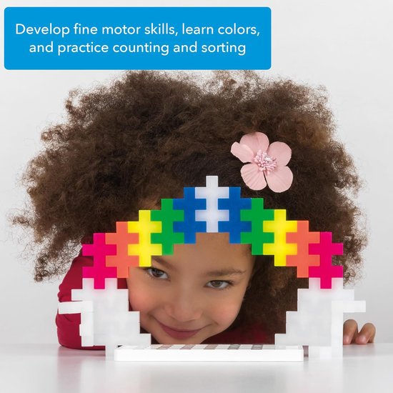 Meisje met krullend haar bouwt een regenboog van Plus-Plus stenen met een witte basis.