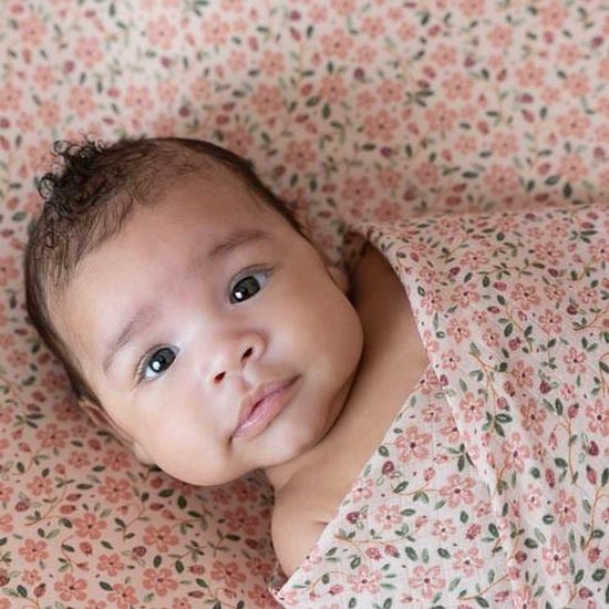 Baby met donker haar, verpakt in een roze hoeslaken met bloemenprint.