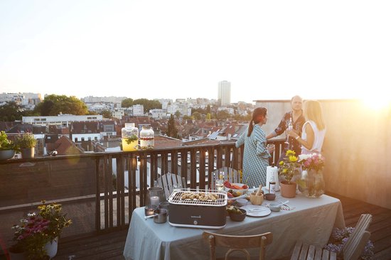 Groep vrienden op een balkon bij zonsondergang rond een tafel met een barbecue.