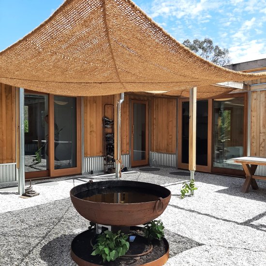 Een modern huis met een patio bedekt met bruine kokosvezel schaduwdoeken.