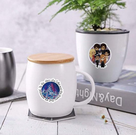 Witte mok en plantenpot versierd met cartoonstickers van personages en bergen.