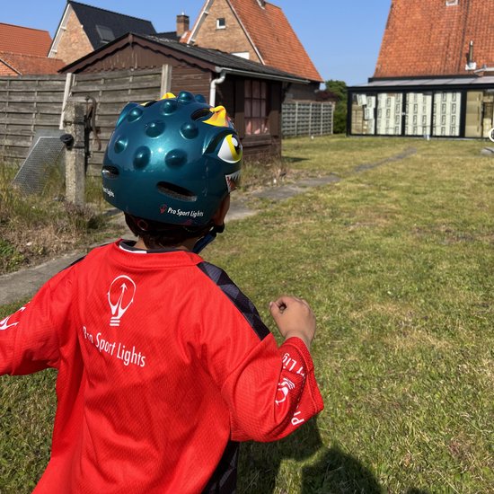 Jongen met groene dinosaurushelm en rood-zwart shirt in de tuin.