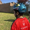 Jongen met groene dinosaurushelm en rood-zwart shirt in de tuin.