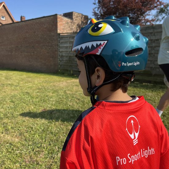 Jongen met groene dinosaurushelm en rood-zwart shirt in de tuin.
