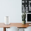 Witte luchtreiniger op een houten bureau met een plant en een kalender aan de muur.
