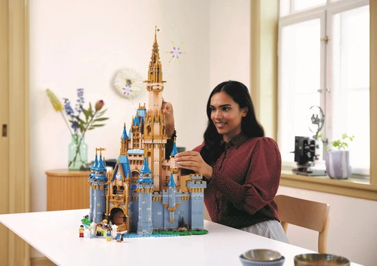 Een vrouw bouwt het LEGO Disney Kasteel in een lichte woonkamer, op een witte tafel.