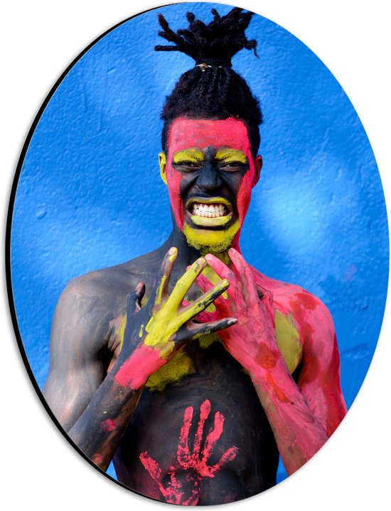 Dibond Ovaal - Man versierd met Rode en Gele Verf tegen Blauwe Muur - 21x28 cm Foto op Ovaal (Met Ophangsysteem)