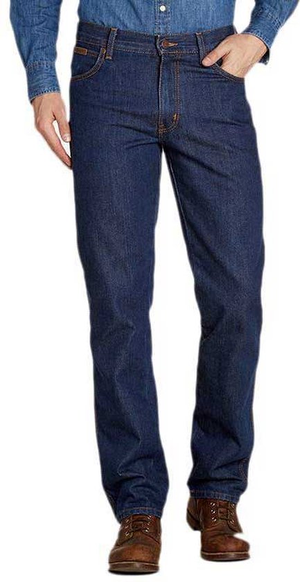 Model draagt een donkerblauwe Wrangler-spijkerbroek met regular fit en bruine leren schoenen.