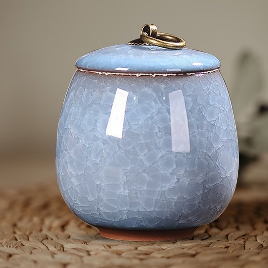 Hemelsblauwe keramische pot met deksel, krakelglazuur en gouden ring, staand op een gevlochten ondergrond.
