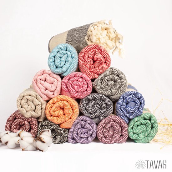 Stapel opgerolde hamamdoeken in verschillende kleuren, waaronder zalmroze en crème, met franjes.