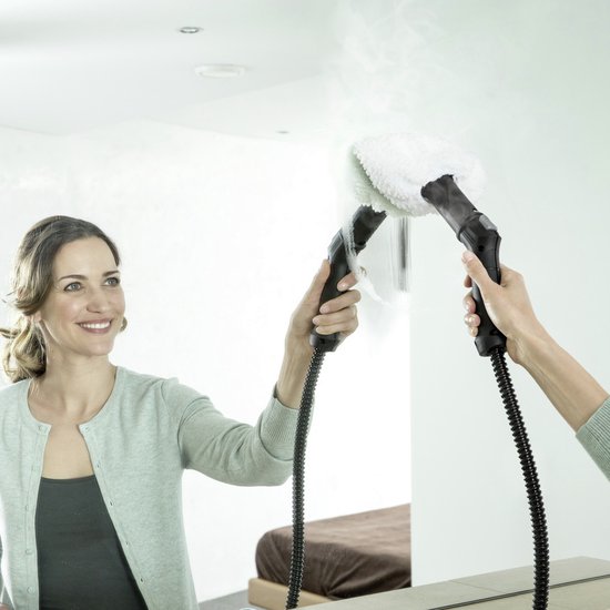 Vrouw gebruikt stoomreiniger op spiegel. Stoom komt van de nozzle.