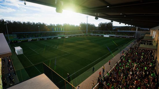 Voetbalstadion met groen veld, tribune met groene accenten en bomen op de achtergrond.