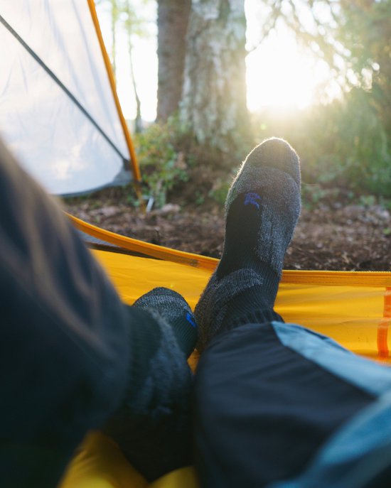 Voeten in donkergrijze wandelsokken in een gele tent bij zonsopgang.