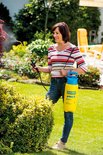 Vrouw sproeit struiken met gele Gloria Prima 5 drukspuit in de tuin.