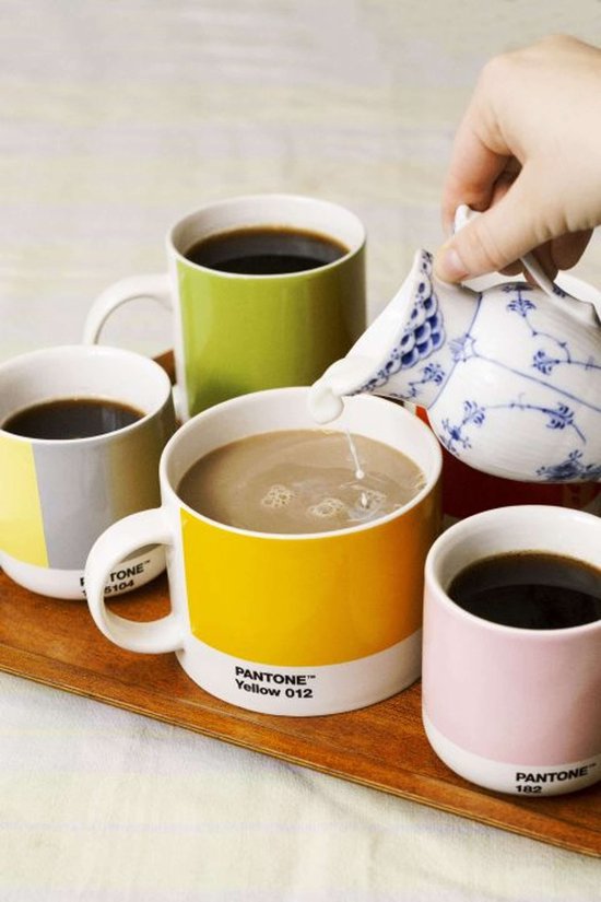 Bovenaanzicht van mokken met koffie, een hand voegt melk toe aan een gele mok.