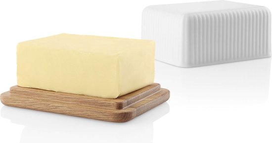Un bloc de beurre sur une planche en chêne, à côté d'un beurrier blanc en porcelaine.