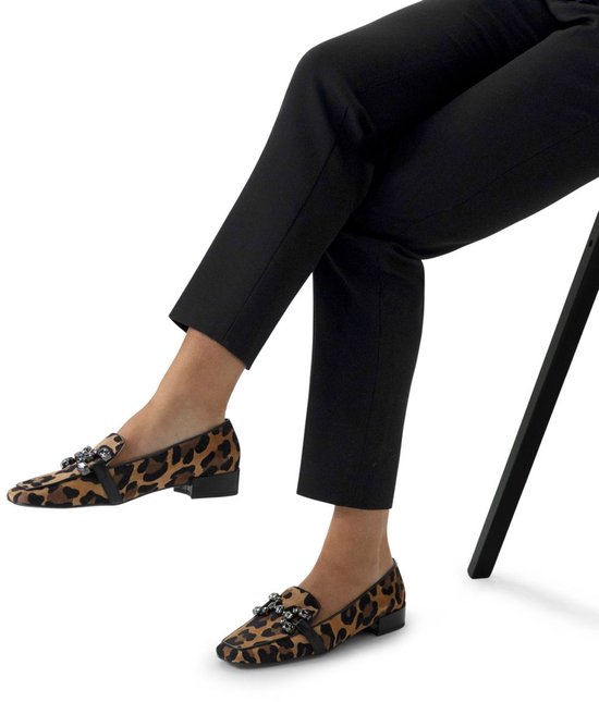 Een vrouw met zwarte broek draagt panterprint instappers met kristallen versiering.