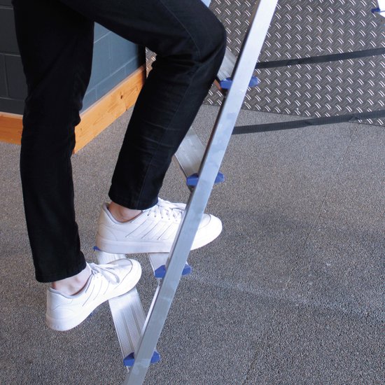 Man in zwarte broek en witte schoenen klimt op zilveren trap met blauwe accenten.