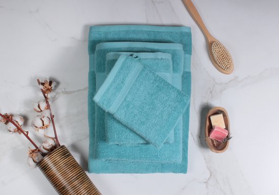 Pile de serviettes bleu clair de différentes tailles sur fond blanc. À côté de la pile se trouvent des branches de coton, une brosse en bois et des savons.