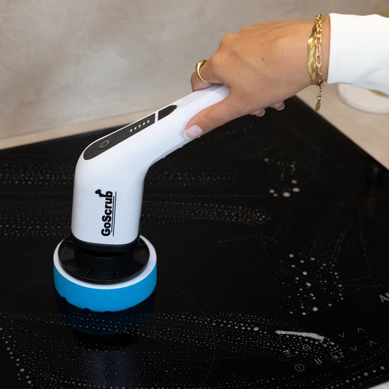 Hand houdt witte GoScrub elektrische schoonmaakborstel met blauwe opzetborstel op een zwarte kookplaat.