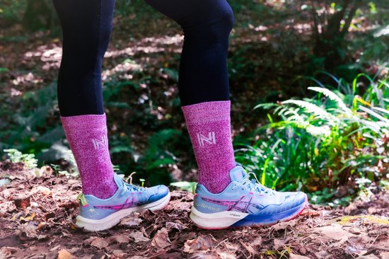 Dichtbij van voeten in roze sokken met 'N' logo en lichtblauwe hardloopschoenen met roze accenten.