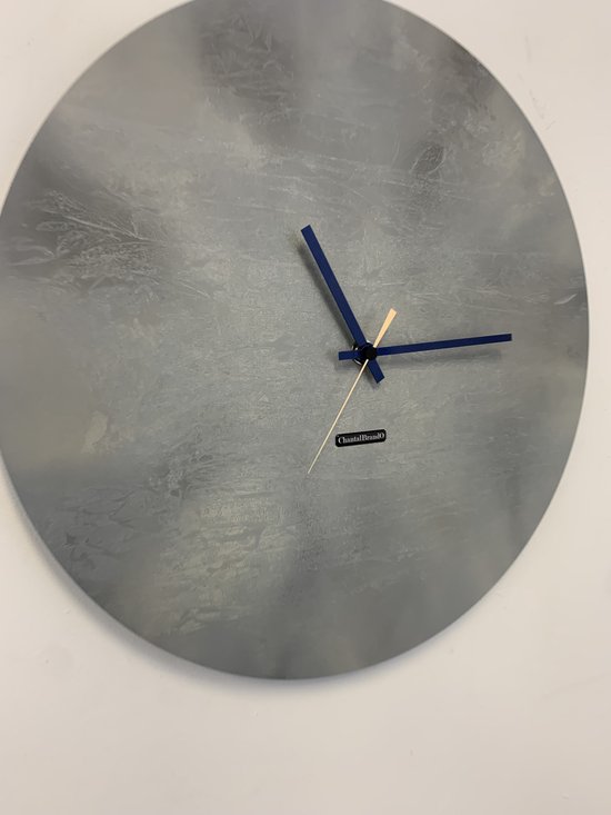 Horloge mural gris à texture craquelée et aiguilles bleu foncé. Nom de marque 'ChantalBrandO'.
