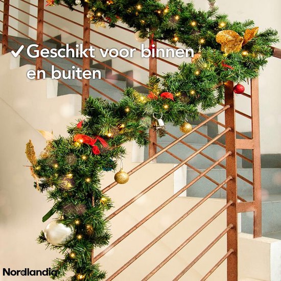 Groene kerstguirlande met warme LED-lampjes en gouden decoraties, om een traphek in huis.