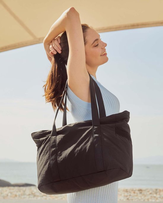 Femme portant un haut bleu clair porte un sac fourre-tout noir au bord de la mer.