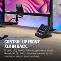 Stream Deck+ met roze knoppen op een houten bureau, met een monitor op de achtergrond.