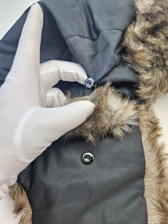 Hand in wit handschoen sluit knoop van donkergrijze pilotenmuts met bruine imitatiebontrand.
